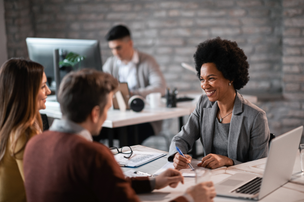 Smiling female at a desk taking notes in a meeting with two customers in an office setting