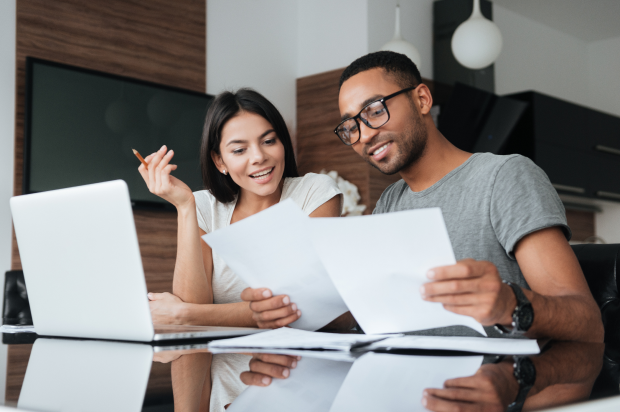 Two coworkers in an office setting reviewing documents with a laptop in front of them