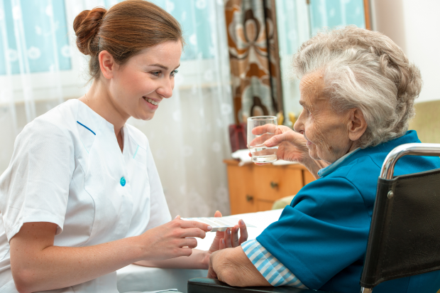 Female nurse smiling at her elderly patient helping her take her medication