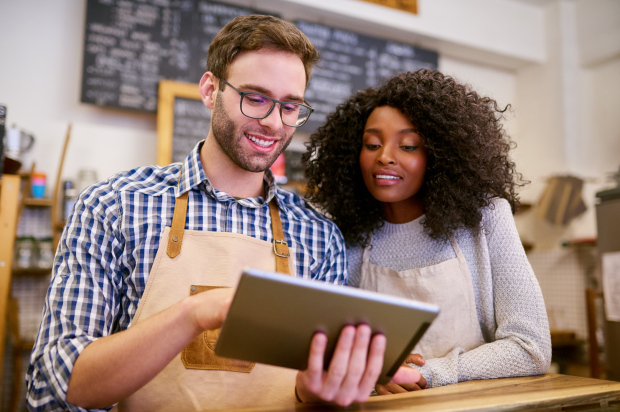 Male and female coffee shop coworkers looking at a tablet