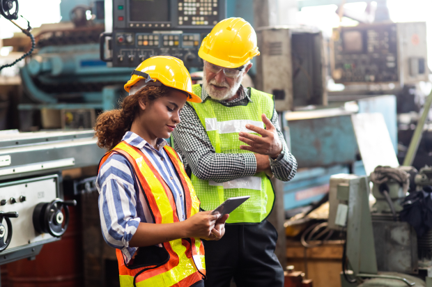 Manufacturing coworkers wearing hardhats and safety vests discussing something on a tablet